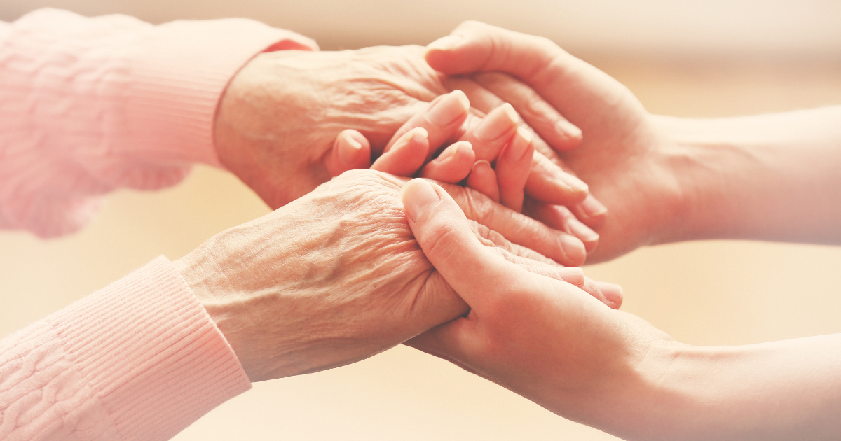 A close-up view of a caregiver’s hands gently holding the hands of an elderly person.