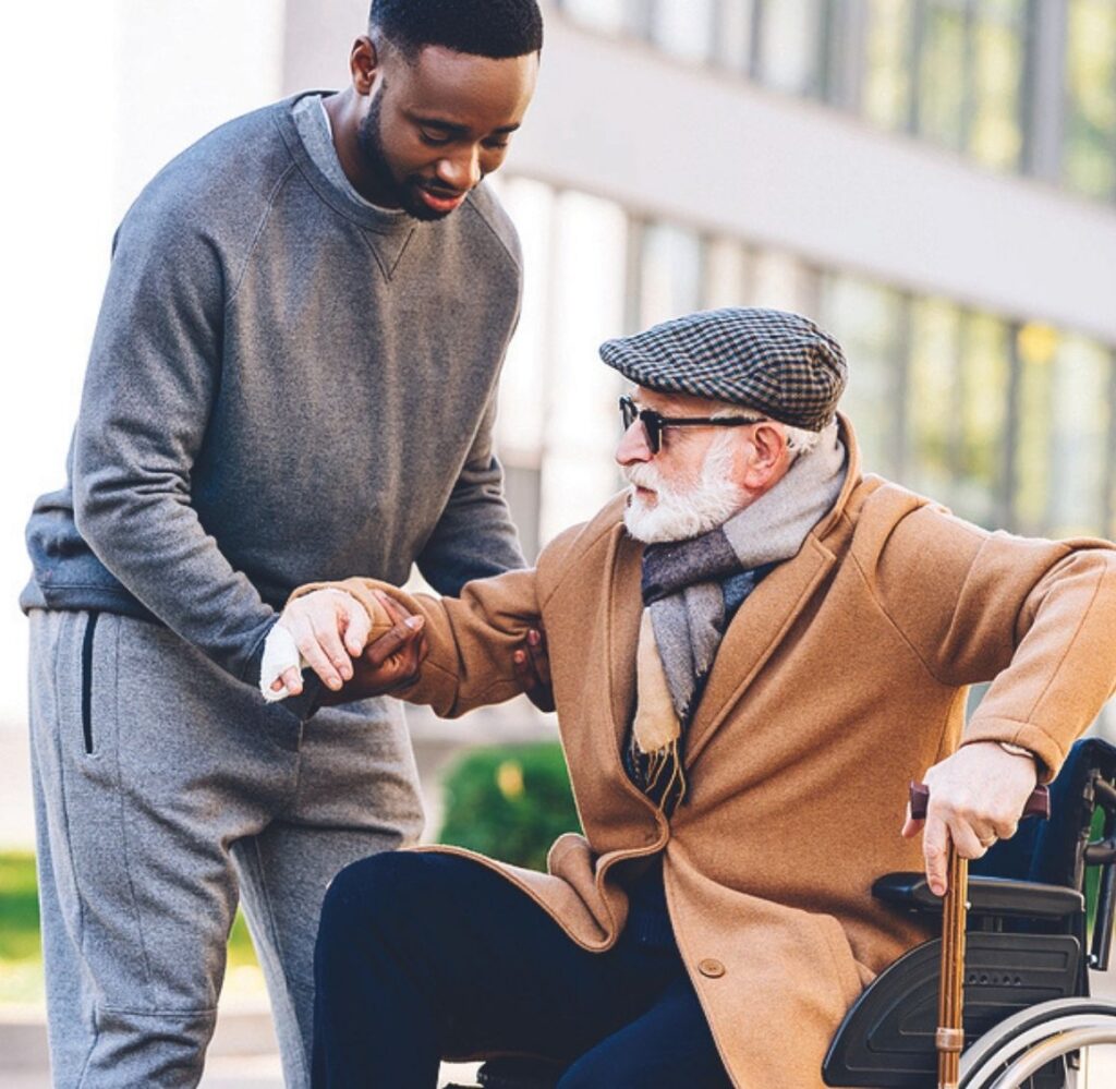 Caregiver Assisting Elderly Man in a Wheelchair Young caregiver helping an elderly man in a wheelchair by supporting his arm outdoors.